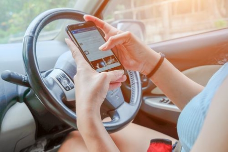 Person using their phone with both hands while sitting behind a steering wheel in a car.